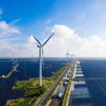 Image of windmills towering over solar farms.