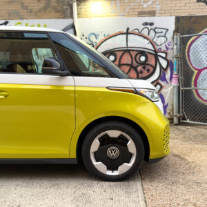 The front of a yellow and white VW ID Buzz parked in an alley with some graffiti.